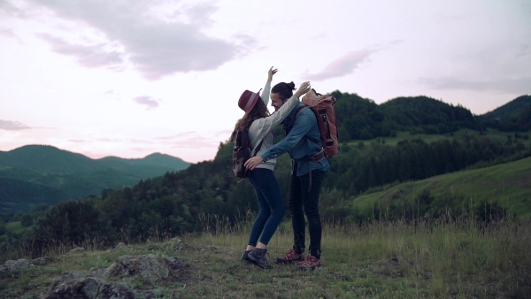 A young tourist couple travellers with backpacks hiking in nature, hugging. Slow motion.