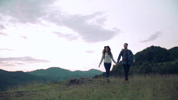 A young tourist couple travellers with backpacks hiking in nature. Slow motion.