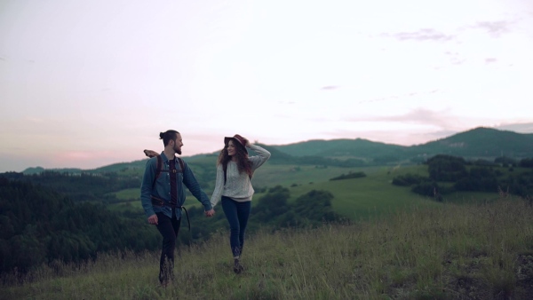 A young tourist couple travellers with backpacks hiking in nature. Slow motion.