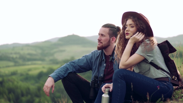 Young tourist couple travellers with binoculars hiking in nature, sitting and resting.