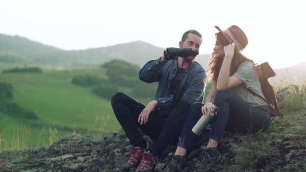 Young tourist couple travellers with binoculars hiking in nature, sitting and resting.