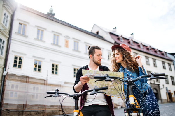 Young tourist couple travellers with map and scooters in small town, sightseeing.