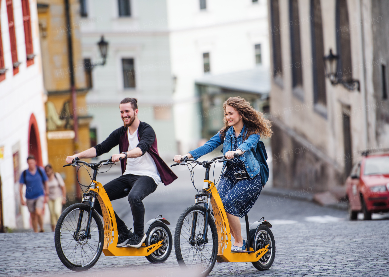 Young tourist couple travellers with electric scooters in small town, sightseeing.