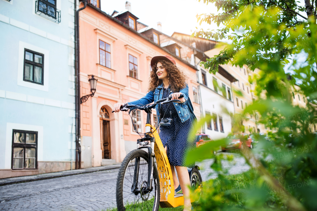 Beautiful young woman tourist traveller with electric scooter in small town, sightseeing.