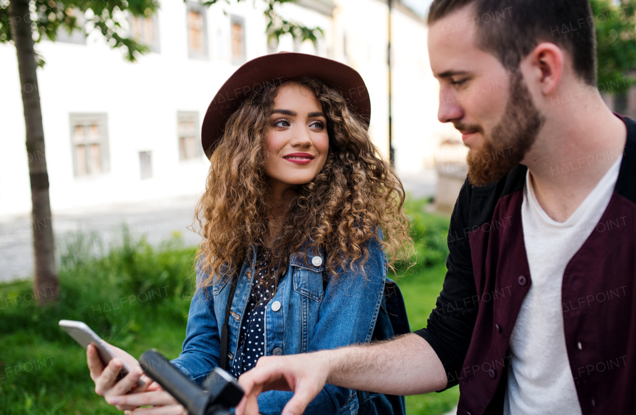 Young tourist couple travellers with smartphone and electric scooters in small town, sightseeing.