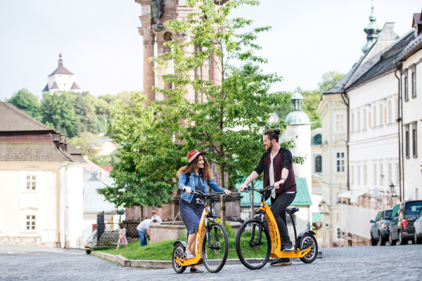 Young tourist couple travellers with electric scooters in a small town, talking.