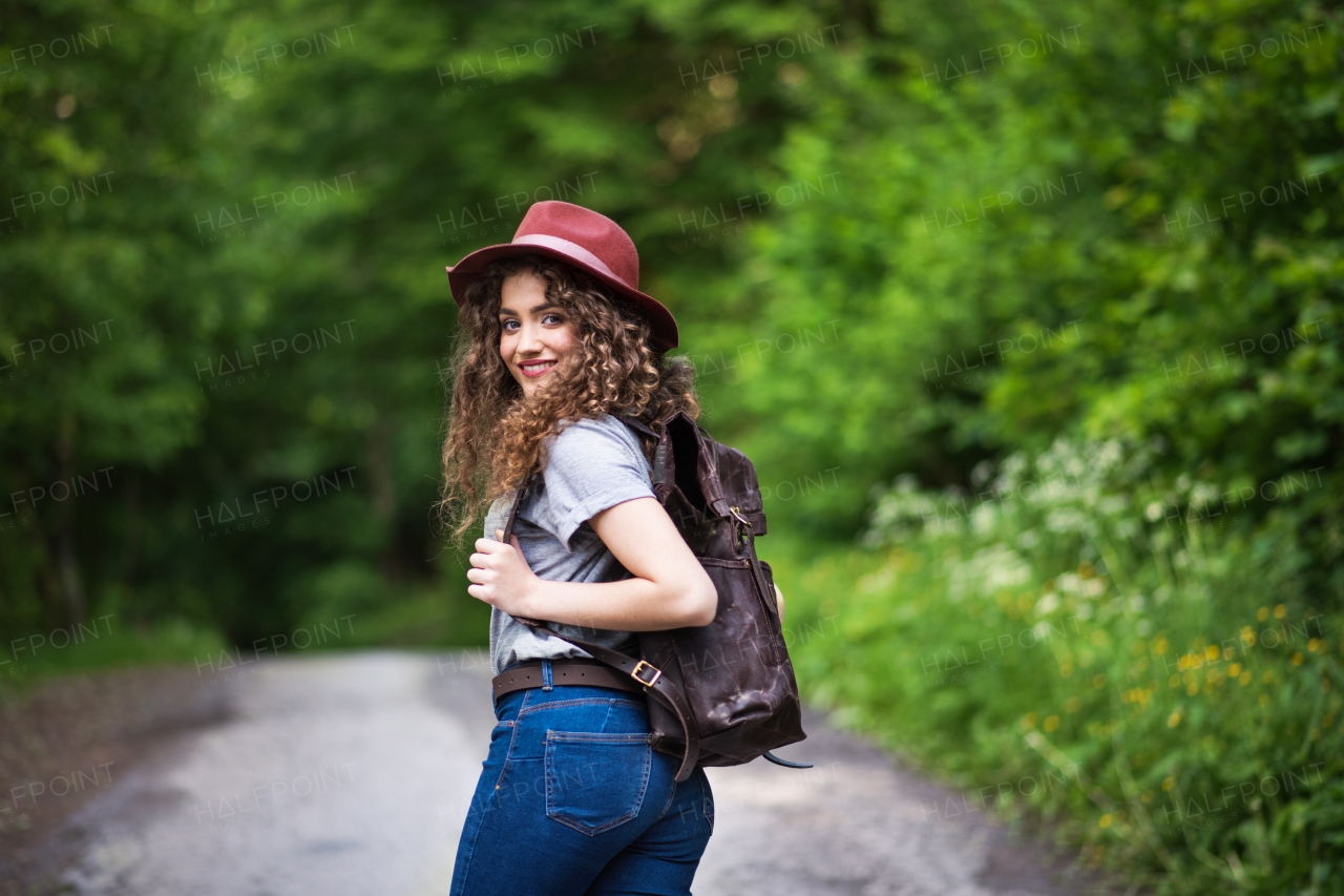 Rear view of young tourist woman traveller with backpack walking in nature, looking back.