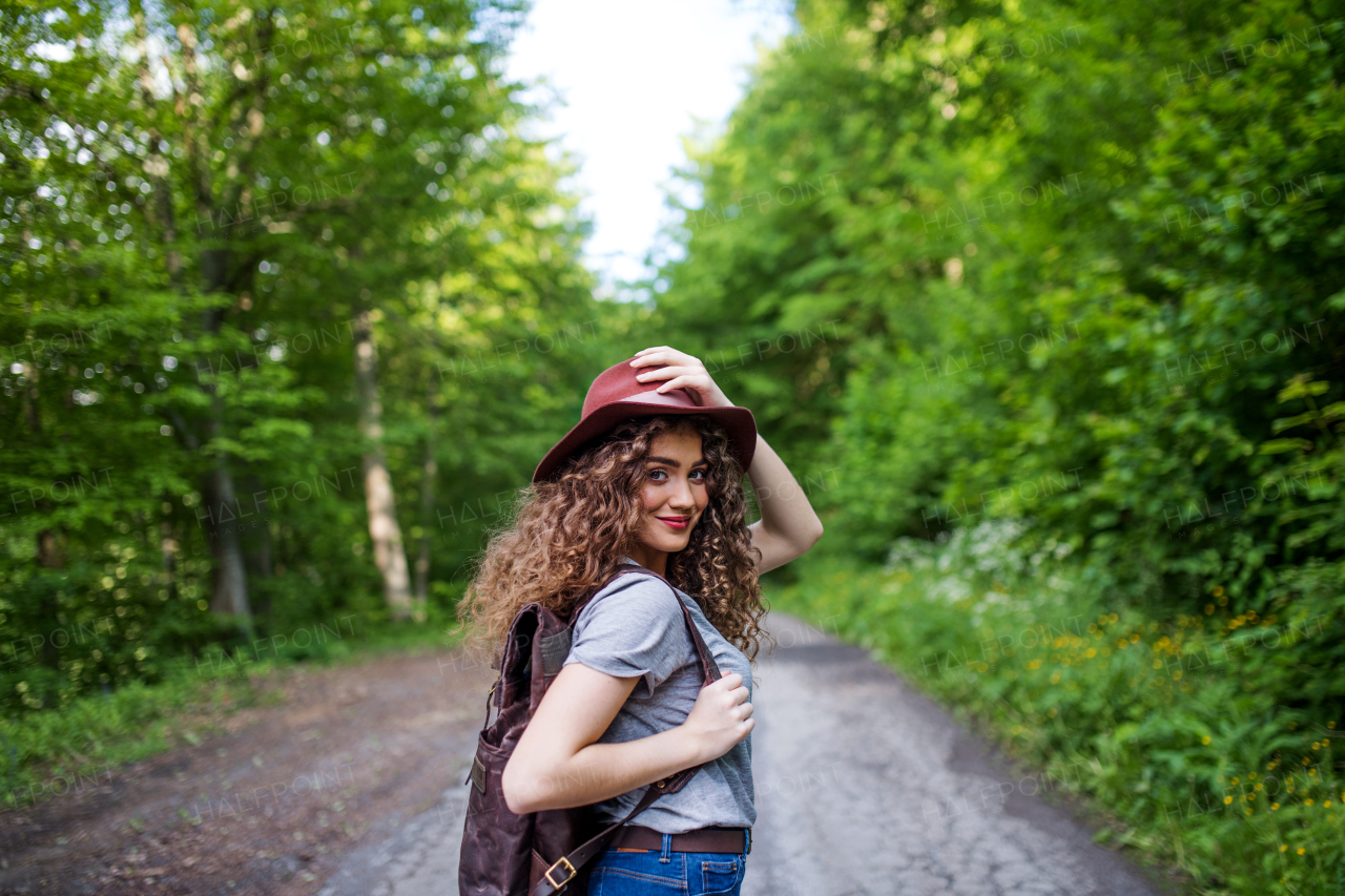 Rear view of young tourist woman traveller with backpack walking in nature, looking back.