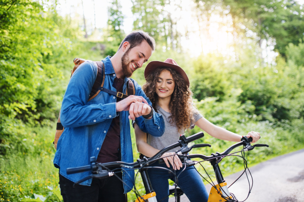 Young tourist couple travellers with backpacks and electric scooters in nature, using smartwatch.