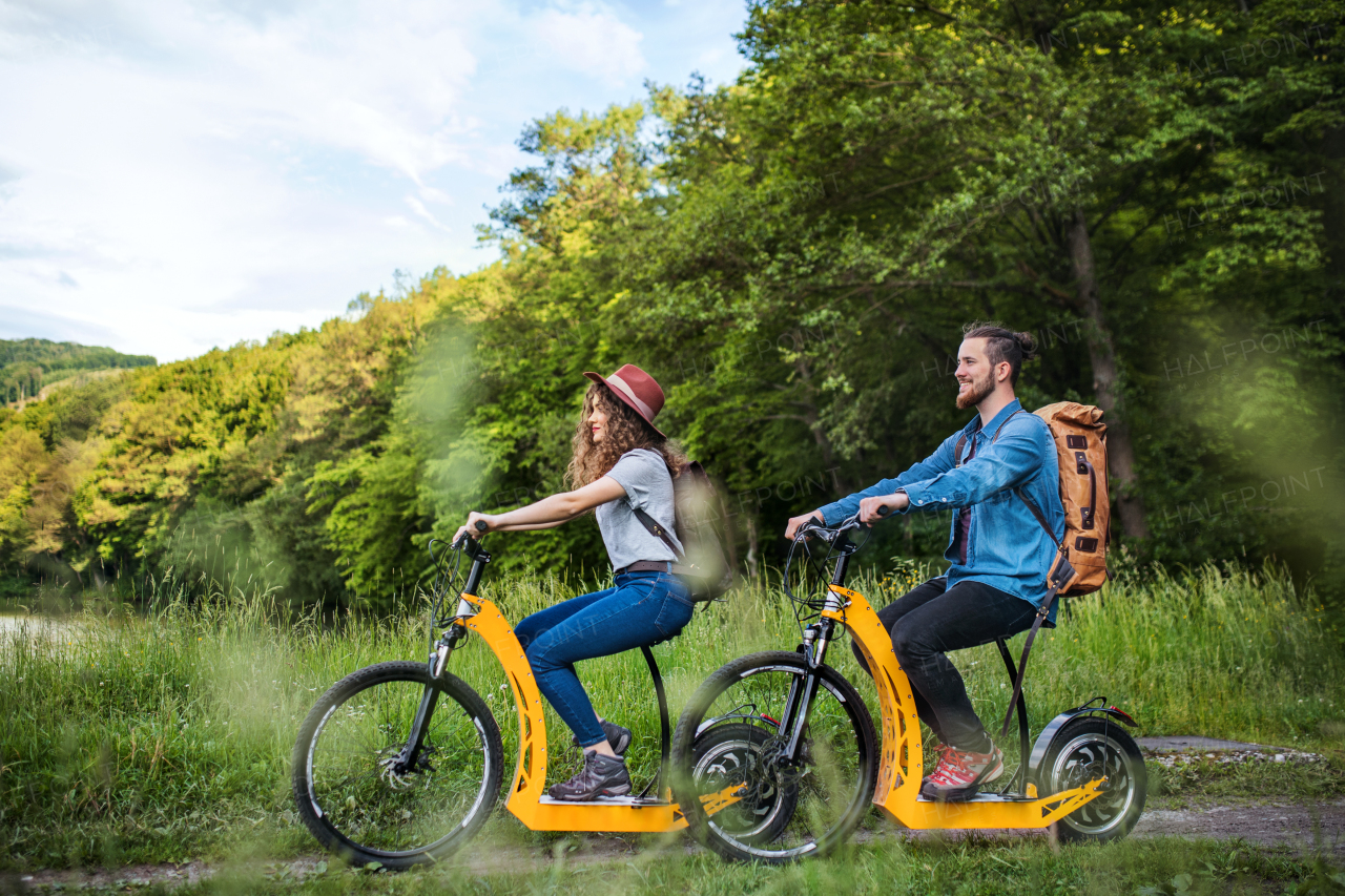 Young tourist couple travellers with backpacks and electric scooters in nature.