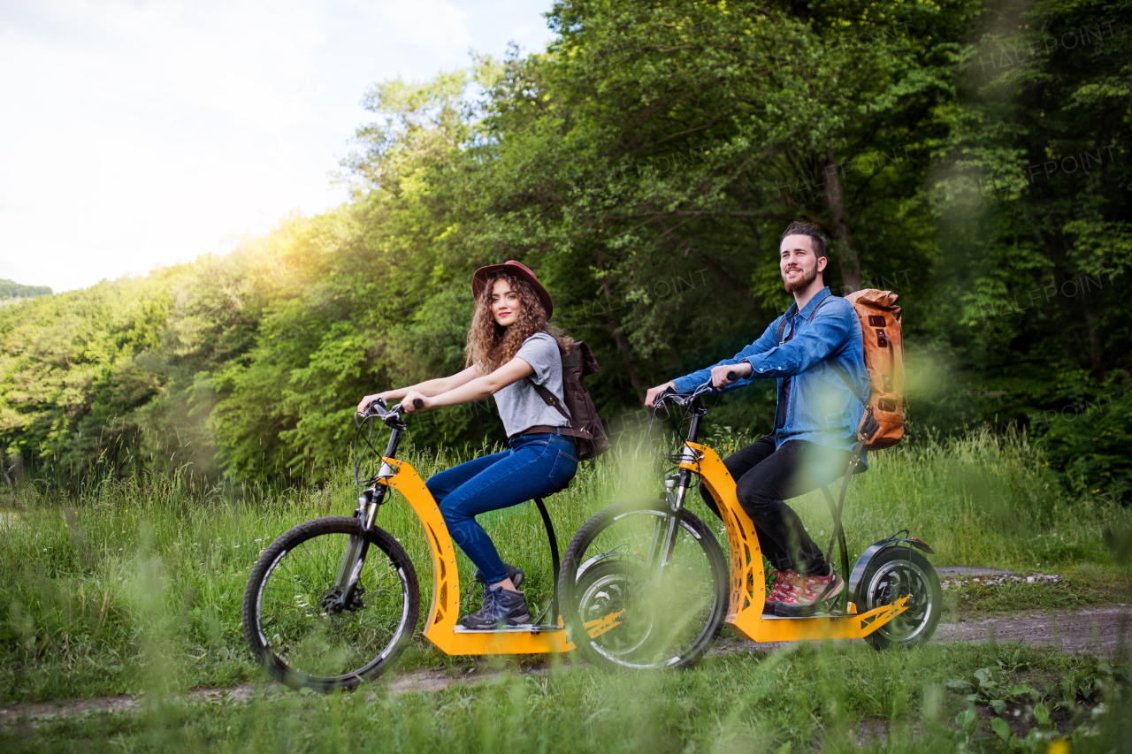 Young tourist couple travellers with backpacks and electric scooters in nature.