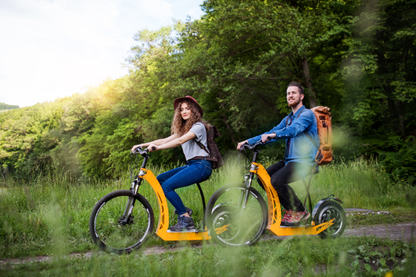 Young tourist couple travellers with backpacks and electric scooters in nature.