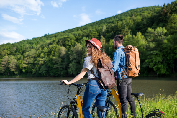 Young tourist couple travellers with electric scooters in nature, standing by lake.