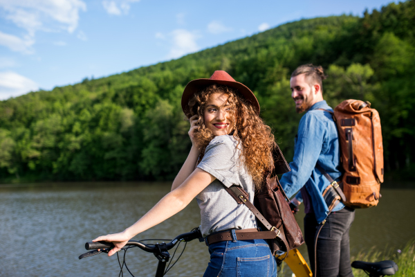 Young tourist couple travellers with electric scooters in nature, standing by lake.