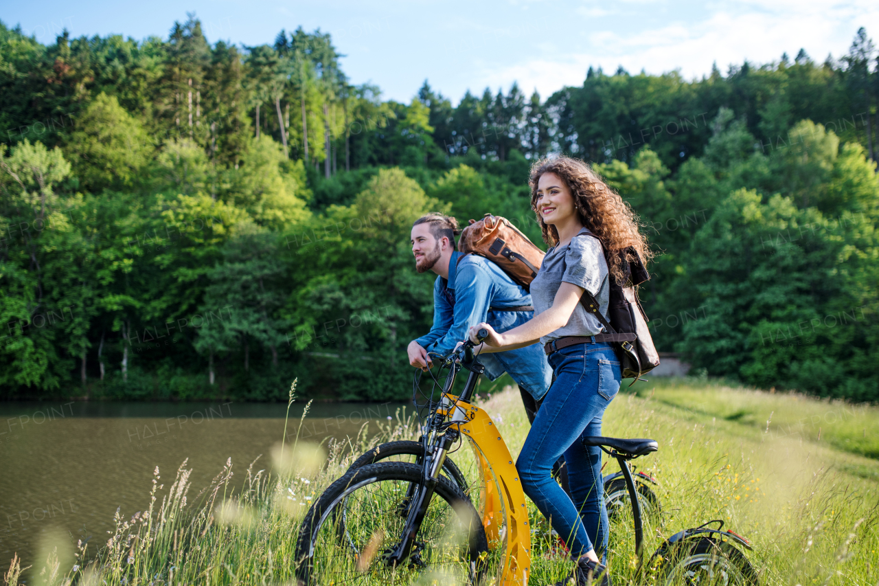 Young tourist couple travellers with electric scooters in nature, standing by lake.