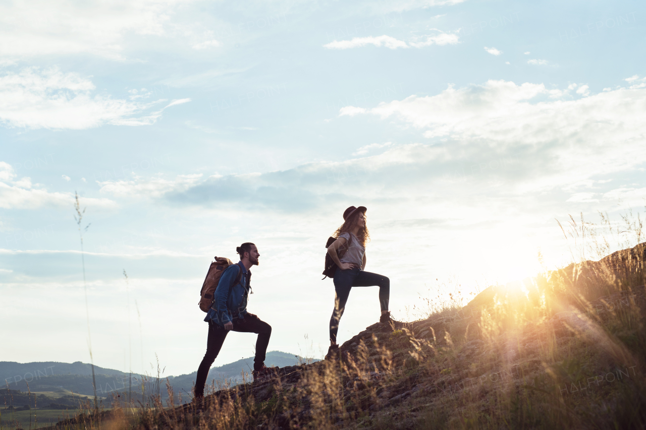 Young tourist couple travellers with backpacks hiking in nature at sunset.