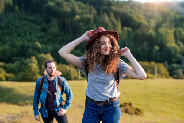 A young tourist couple travellers with backpacks hiking in nature.