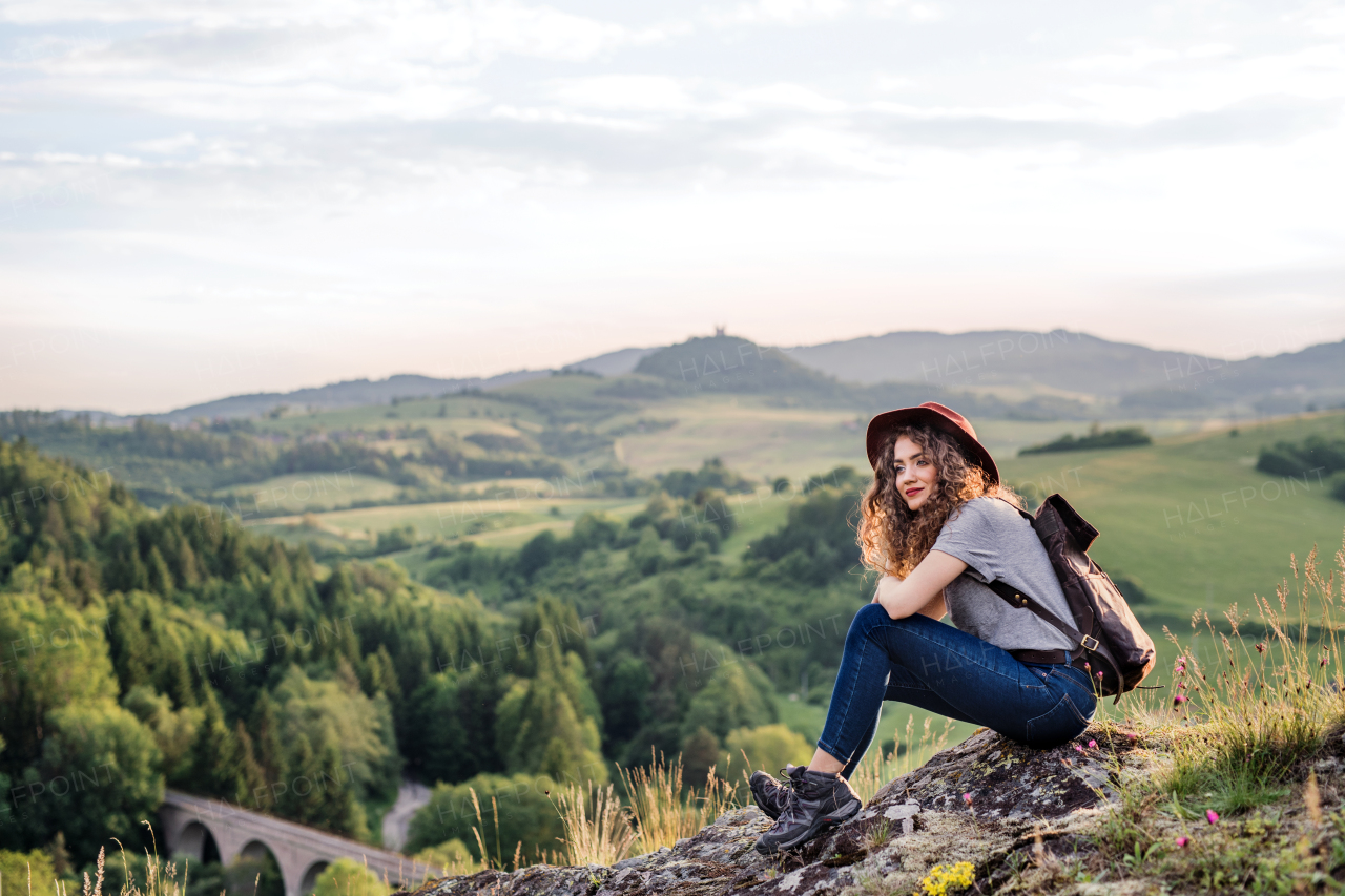 A young tourist woman traveller with backpack sitting in nature. Copy space.