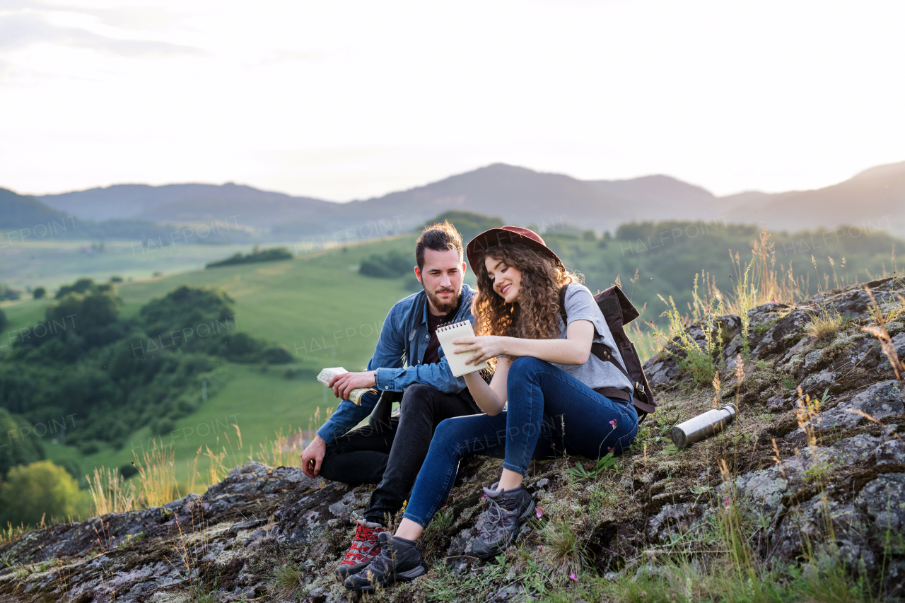 A young tourist couple travellers sitting in nature, resting after hiking.