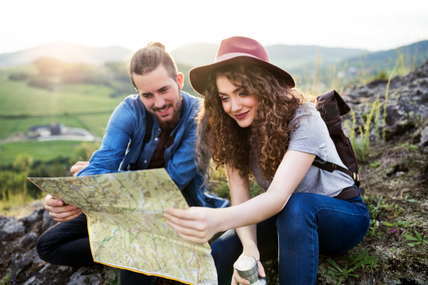 A young tourist couple travellers with backpacks hiking in nature, using map.