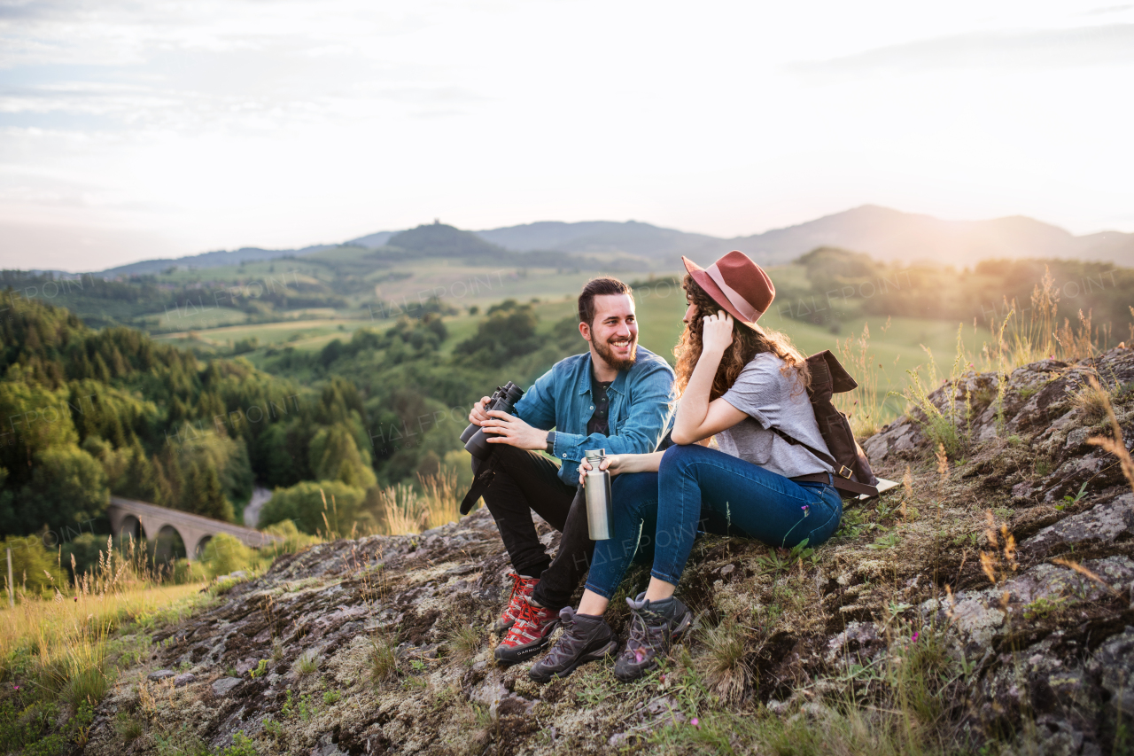 Young tourist couple travellers with binoculars hiking in nature, sitting and resting.