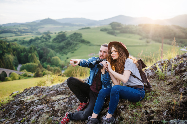 Young tourist couple travellers with binoculars hiking in nature, sitting and resting.