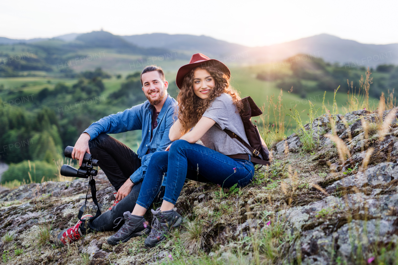 Young tourist couple travellers with binoculars hiking in nature, sitting and resting.