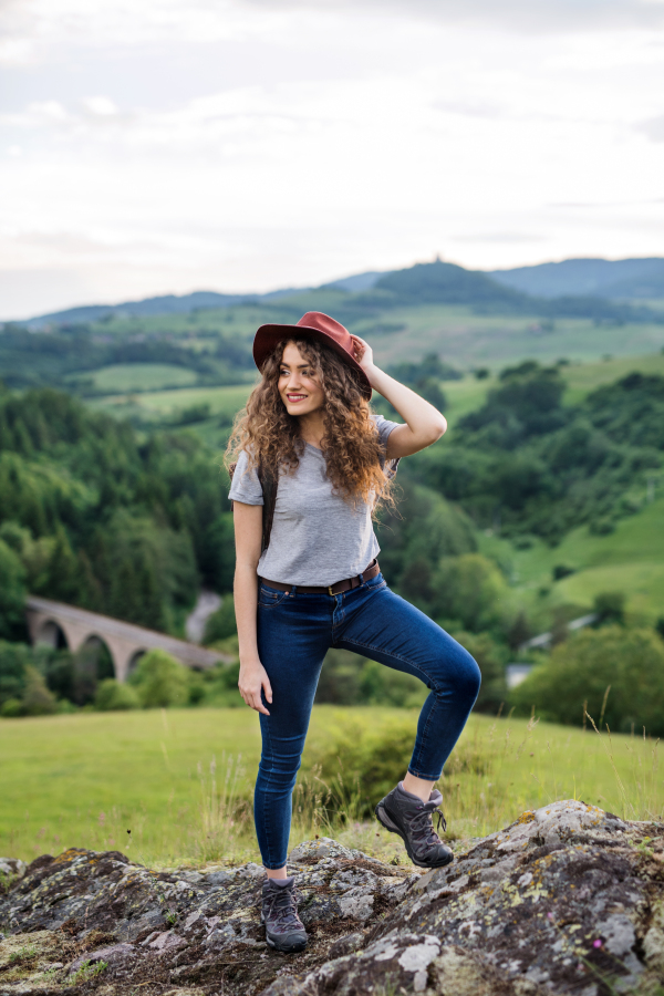 Happy young tourist woman hiker with backpack standing in nature, resting.