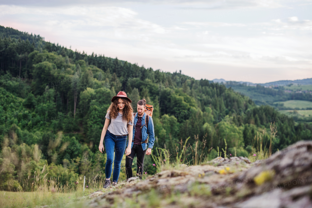 Front view of young tourist couple travellers with backpacks hiking in nature.