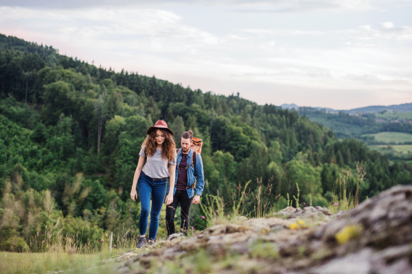 Front view of young tourist couple travellers with backpacks hiking in nature.