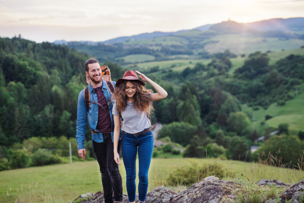 Young tourist couple travellers with backpacks hiking in nature at sunset.