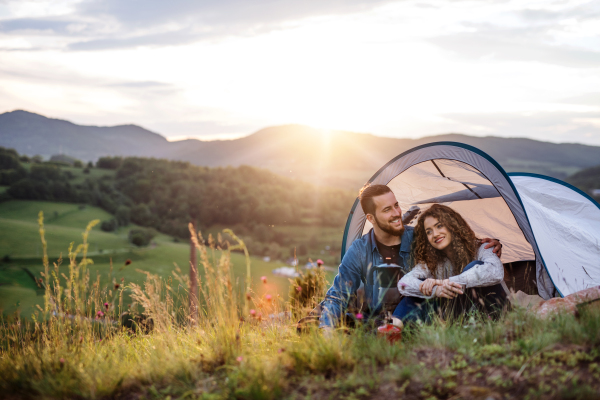 A young tourist couple travellers with tent shelter sitting in nature, drinking coffee.