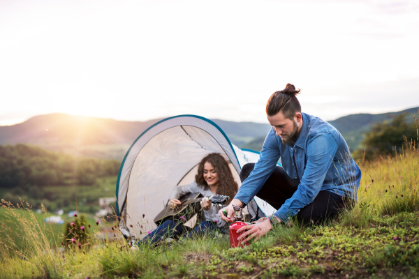 A young tourist couple travellers with tent shelter sitting in nature, resting.