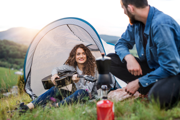 A young tourist couple travellers with tent shelter sitting in nature, playing guitair.