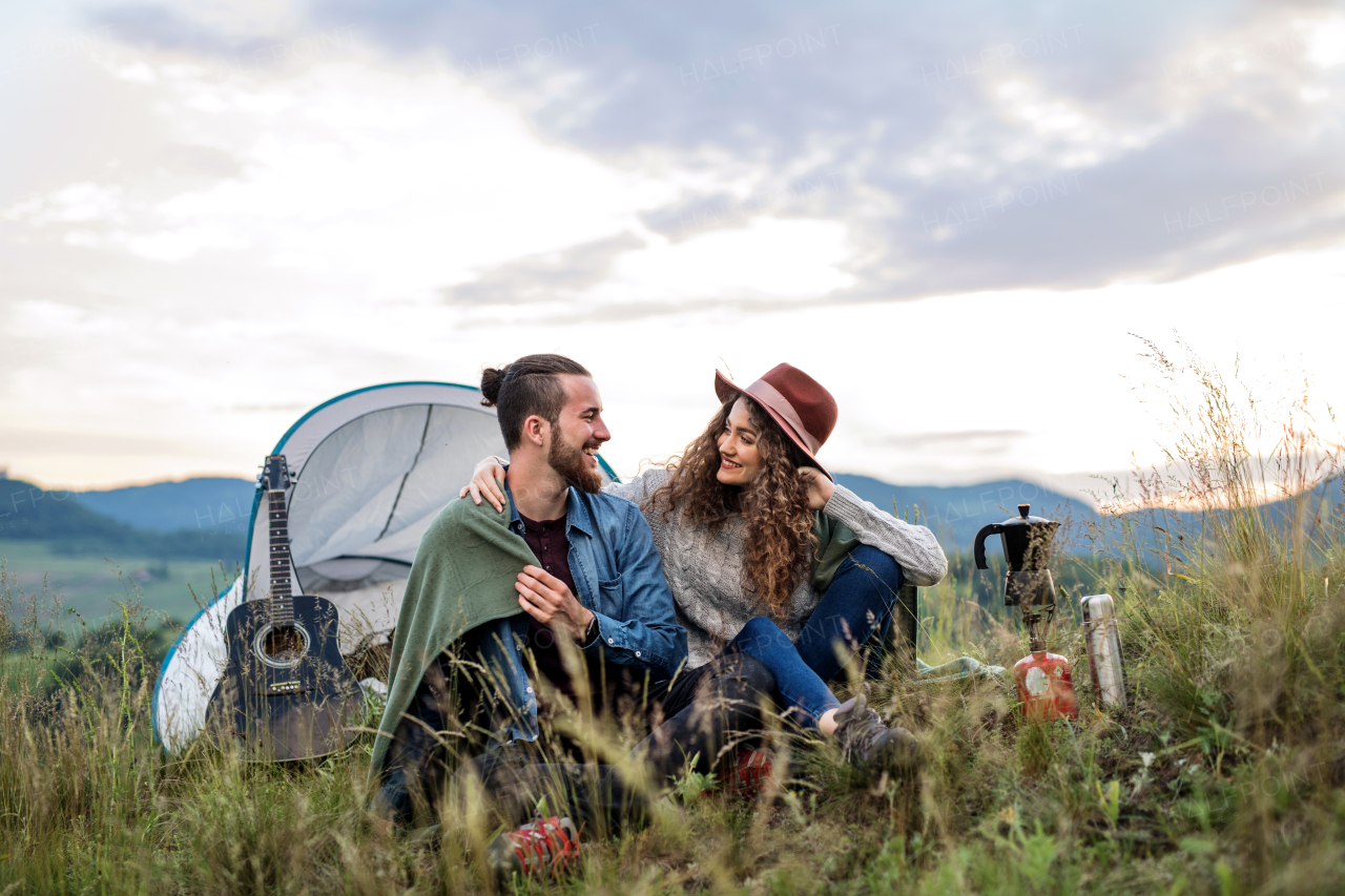 A young tourist couple travellers with tent shelter sitting in nature, resting.