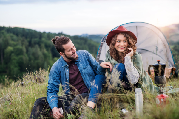 A young tourist couple travellers with tent shelter sitting in nature, resting.