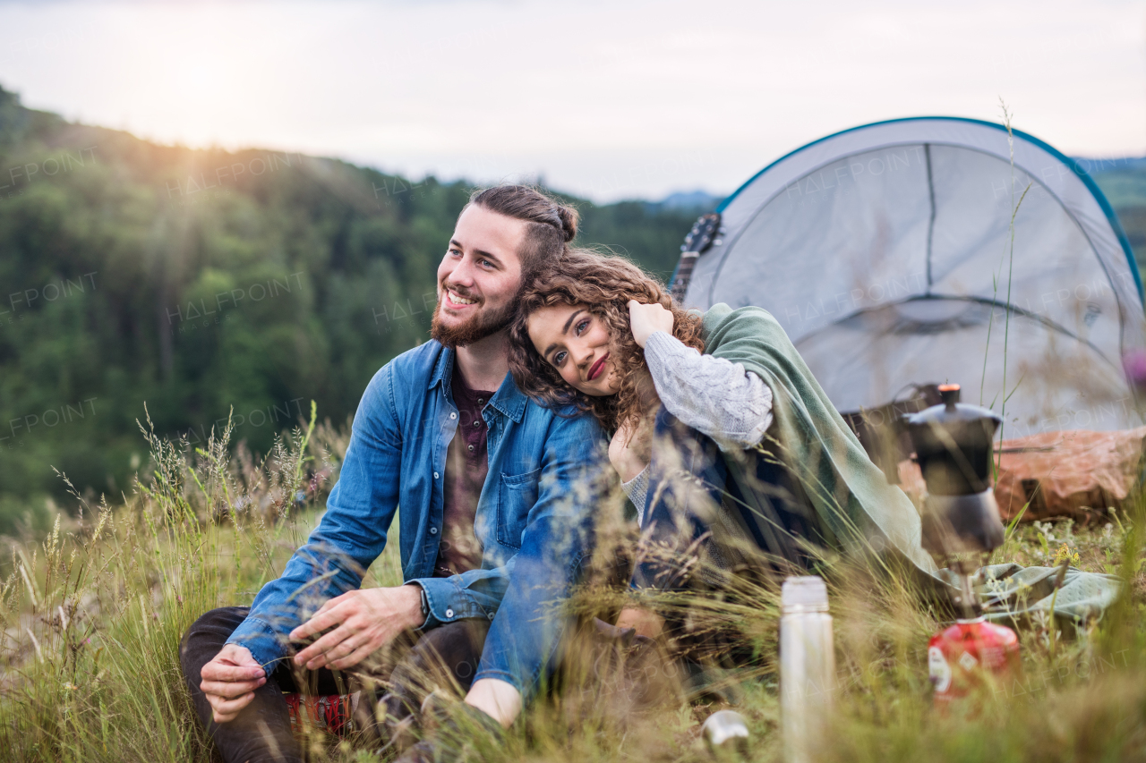 A young tourist couple travellers with tent shelter sitting in nature, resting.