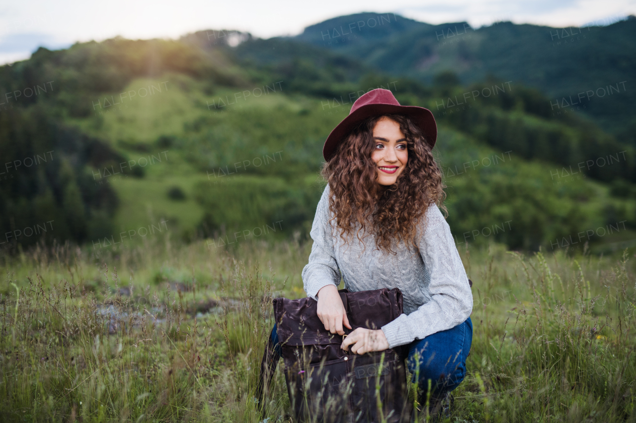 A young tourist woman traveller with backpack sitting in nature, resting.