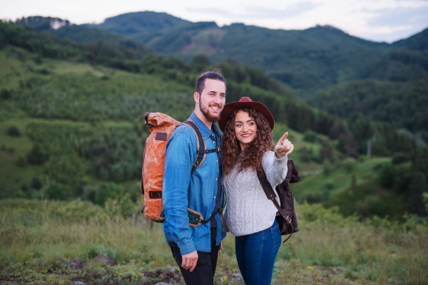 A young tourist couple travellers with backpacks hiking in nature, talking.