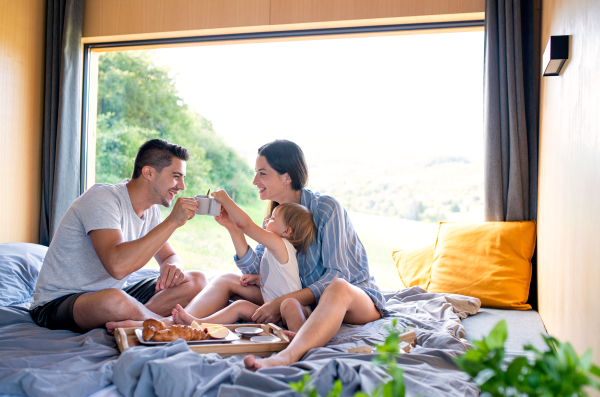 Young couple with small daughter eating breakfast indoors, weekend away in container house in countryside.