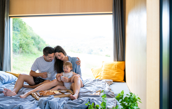 Young couple with small daughter eating breakfast indoors, weekend away in container house in countryside.