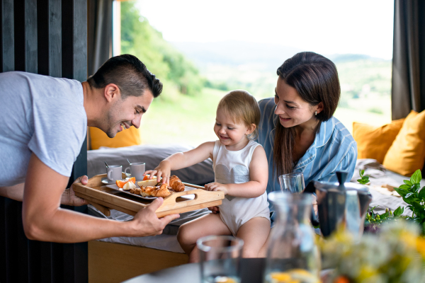 Young couple with small daughter eating breakfast indoors, weekend away in container house in countryside.