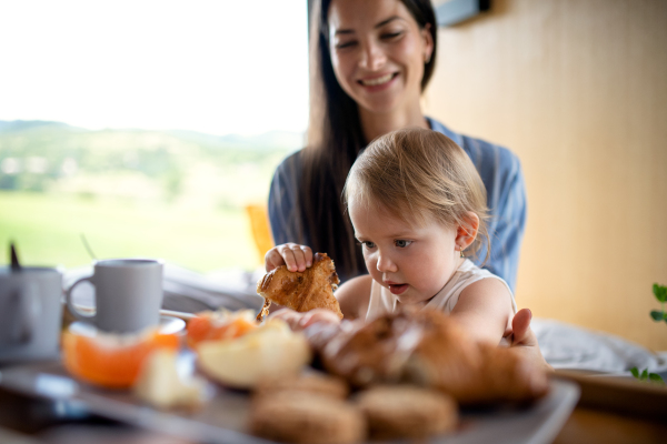 Young woman with small daughter eating breakfast indoors, weekend away in container house in countryside.