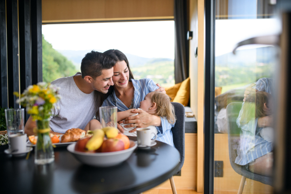 Young family with small daughter sitting indoors, weekend away in container house in countryside.