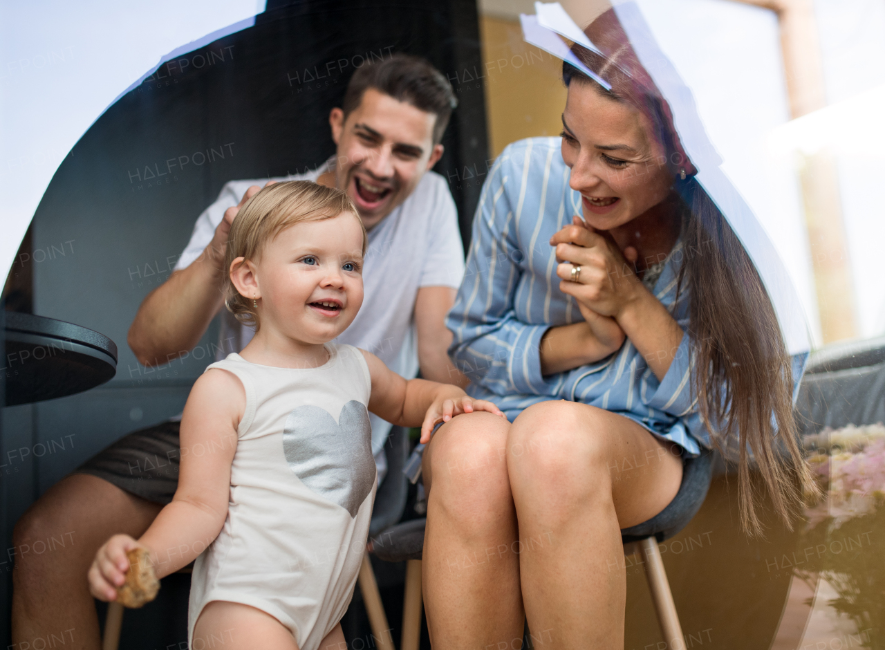 Happy young woman with husband and baby indoors, weekend away in container house in countryside. Shot through glass.