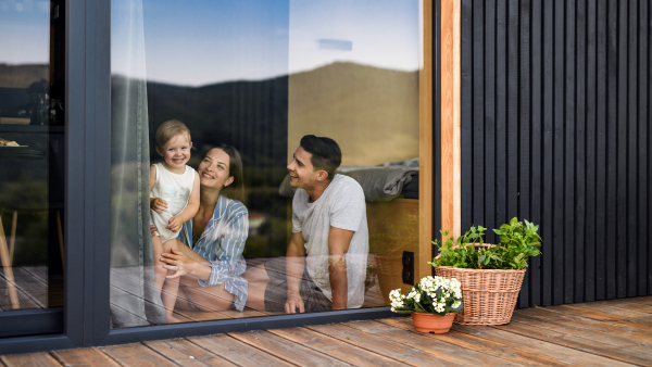 Young family with small daughter indoors, weekend away in container house in countryside. Shot through glass.