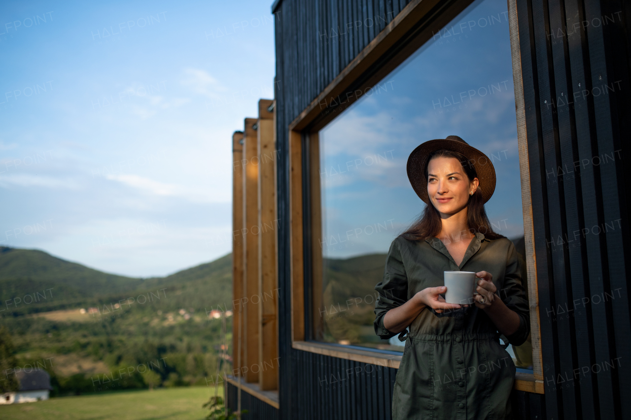 Young woman with coffee outdoors, weekend away in container house in countryside.