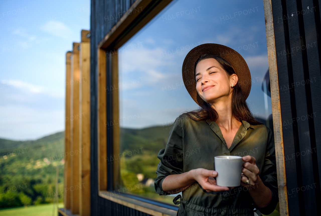 Young woman with coffee outdoors, weekend away in container house in countryside.