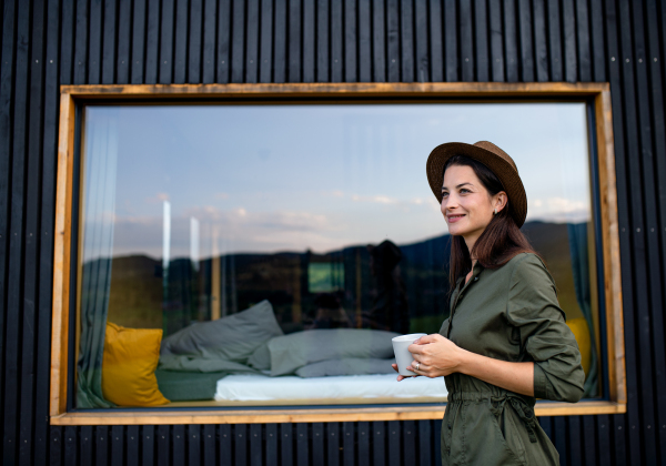 Young woman with coffee outdoors, weekend away in container house in countryside.