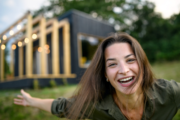 Young woman looking at camera outdoors, weekend away in container house in countryside.